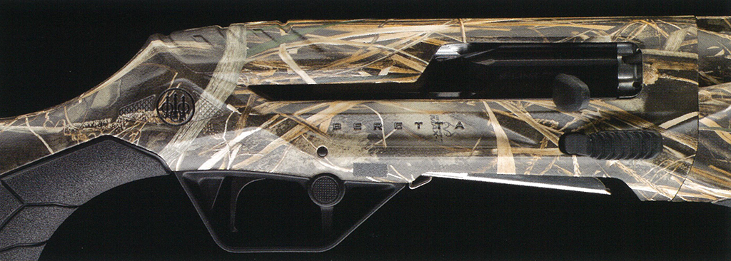 Real tree MAX7 – f-range 東京表参道の銃砲店 Camouflage-pattern hunting shotgun resting on a dark background, side view showing the receiver and trigger area.